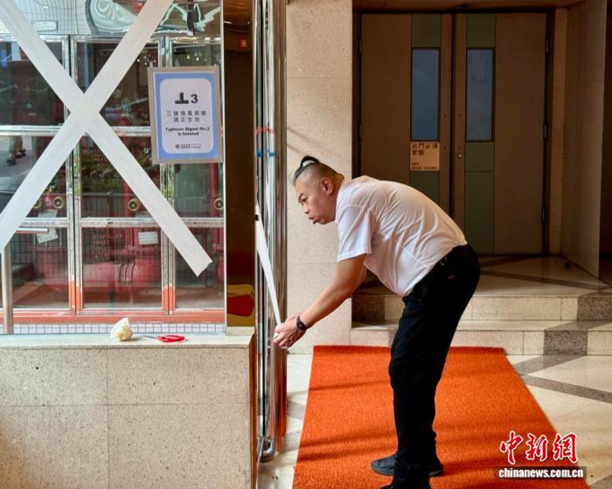 Nhân viên ban quản lý một khu dân cư tại Hồng Kông sử dụng băng dính gia cố cửa ra vào và cửa sổ trước bão Wipha. Ảnh: Chinanews.