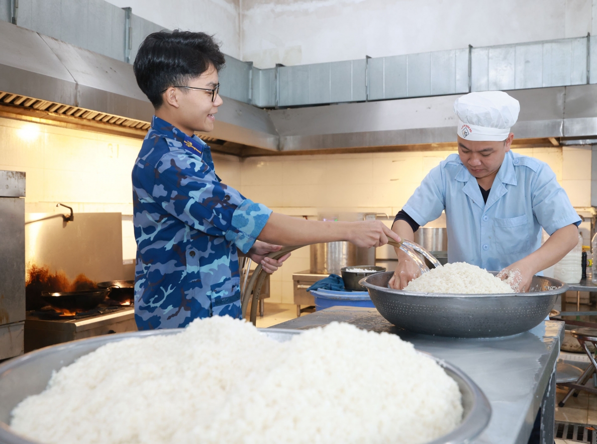 Hạ sĩ Phạm Trọng Đại (đứng) hỗ trợ đồng đội chuẩn bị gạo trước khi cho vào nồi hơi.