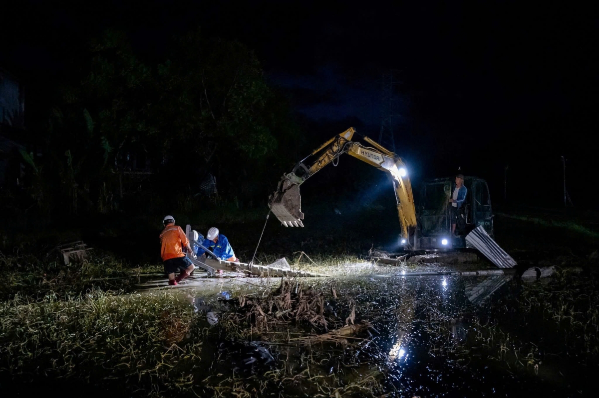 Các công nhân sử dụng máy múc để nâng lại cột bị lũ cuốn đổ.