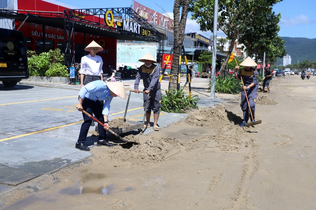 Nhân viên các nhà hàng, khách sạn dọc đường Võ Nguyên Giáp-Hoàng Sa thu dọn cát biển tràn lấp đường.