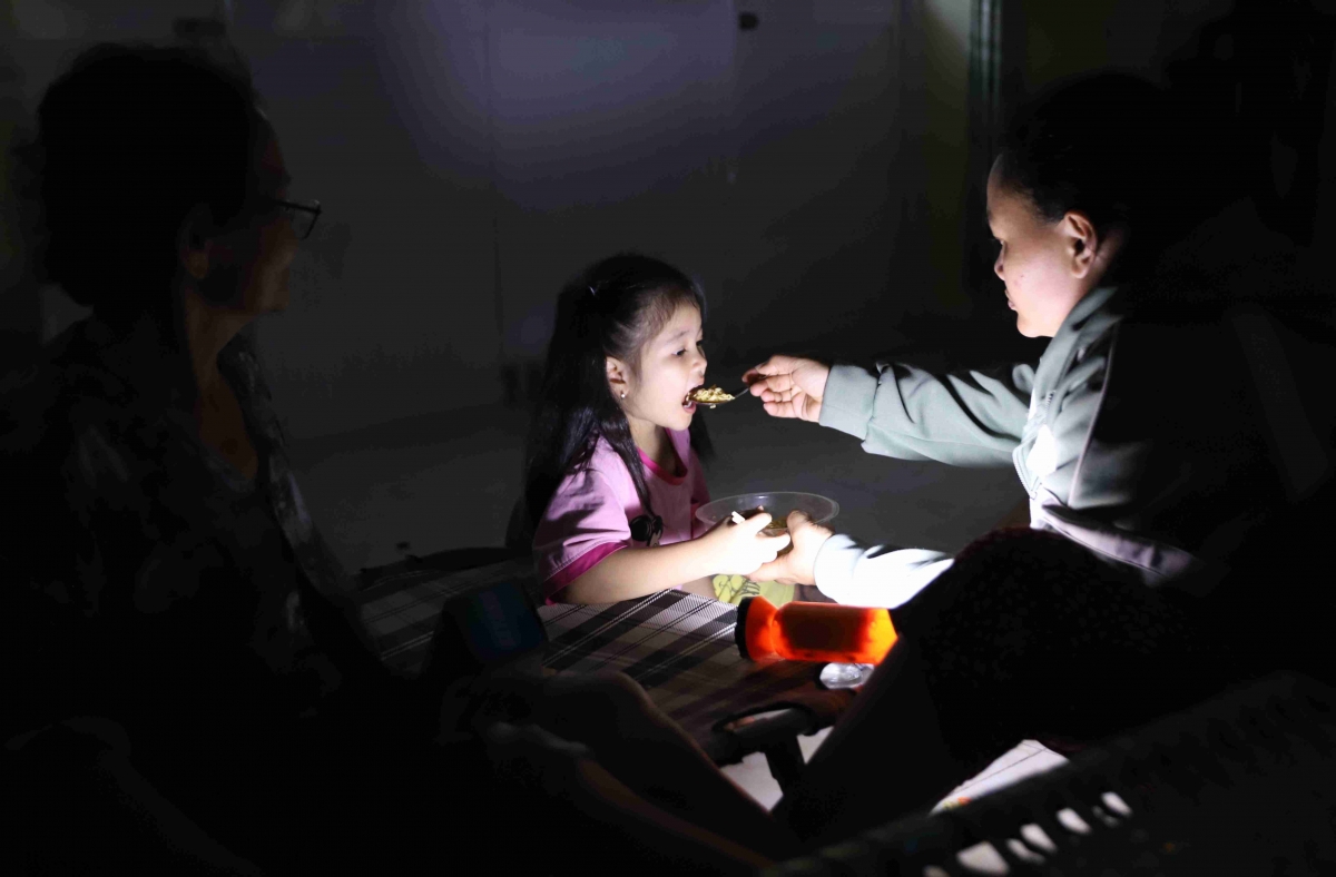 Một người mẹ trẻ ở phường Xuân Đài, tỉnh Đắk Lắk đút mì tôm cho con gái nhỏ ăn. Do mất điện, nên hai mẹ con sử dụng đèn pin để thắp sáng.