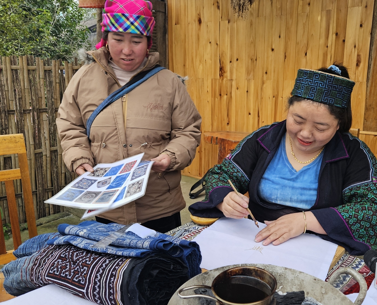 Chị Sùng Thị Lan và các chị em trong bản hướng dẫn du khách các khâu vẽ hoa văn bằng sáp ong trên vải