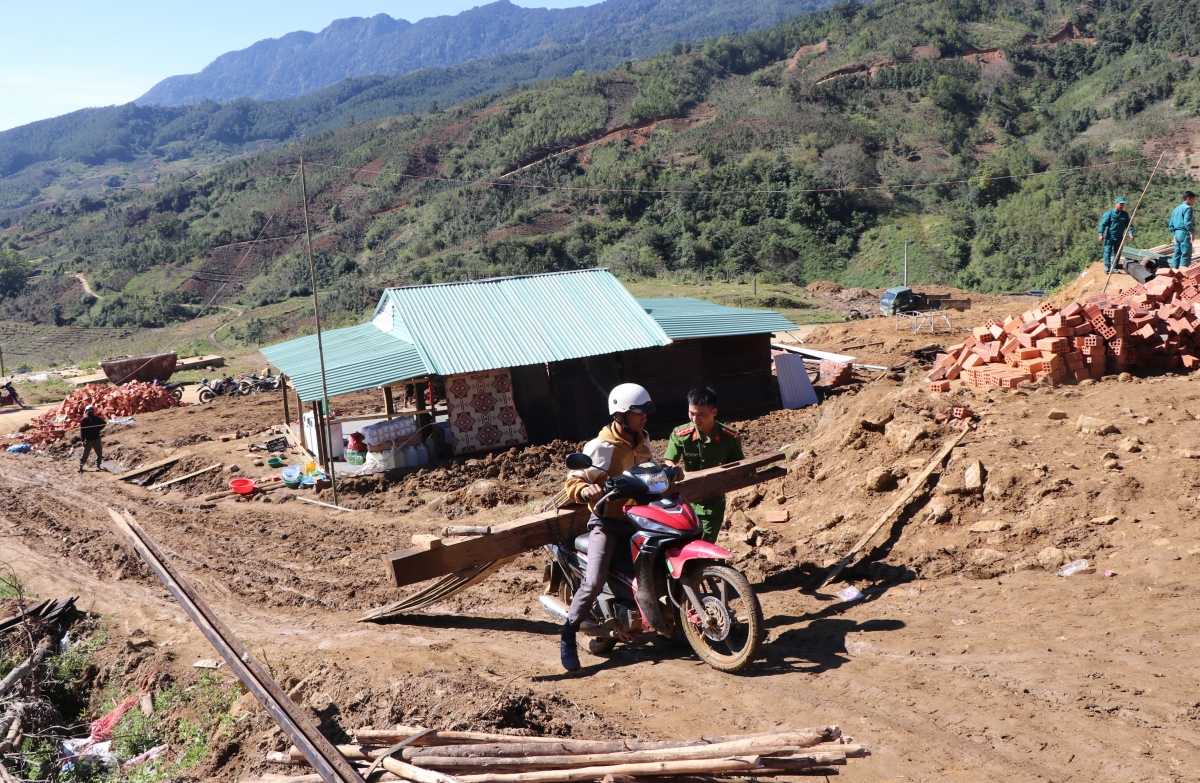 Cán bộ Công an xã Măng Ri hỗ trợ người dân tháo dỡ nhà cũ vận chuyển đến nơi ở mới.