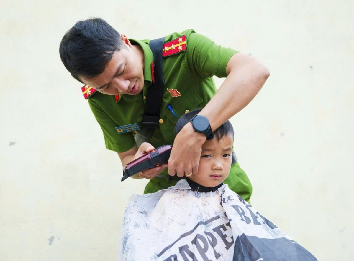 Đại úy Hoàng Xuân Hào, Phó Trưởng Công an xã Bằng Thành cắt tóc cho các cháu nhỏ ở Slam Vè.